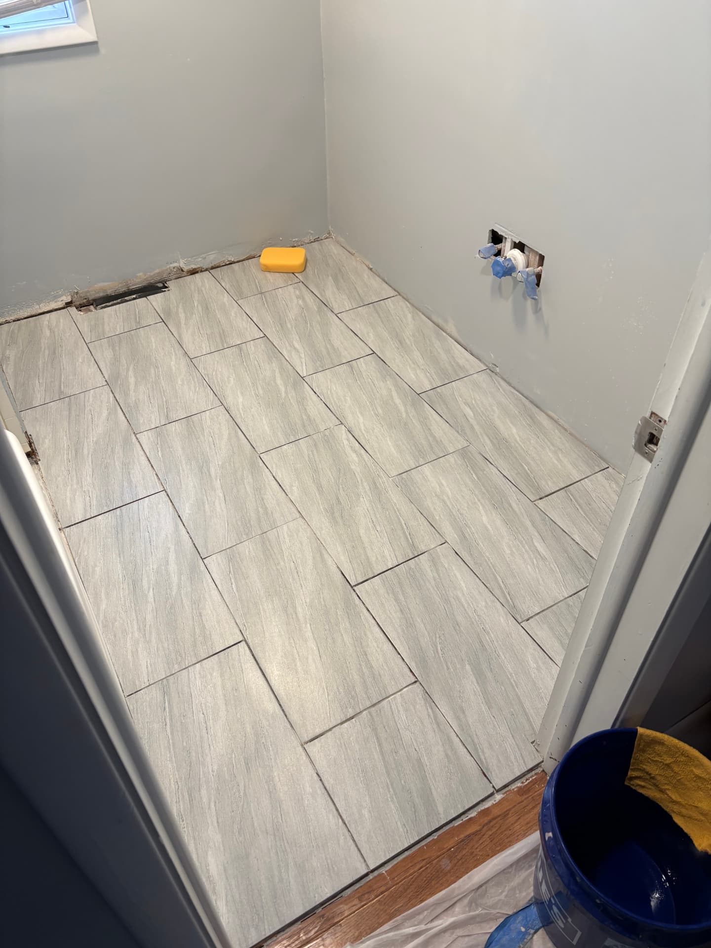 Newly installed gray porcelain tile floor laid in an offset pattern in a small laundry room
